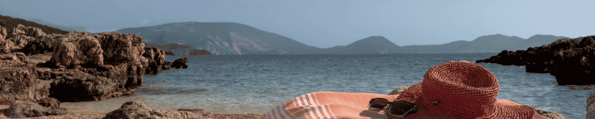 handdoek met hoed en zonnebril erop, liggend op een klein strandje met rotsen