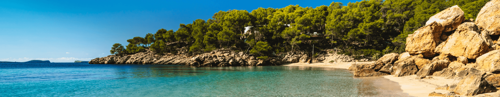 Blauw water, licht beige rotsen en groene bomen