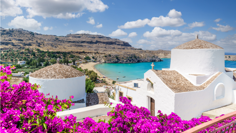 Uitzicht op een typisch Grieks wit kerkje met roze bloemen en helderblauwe zee