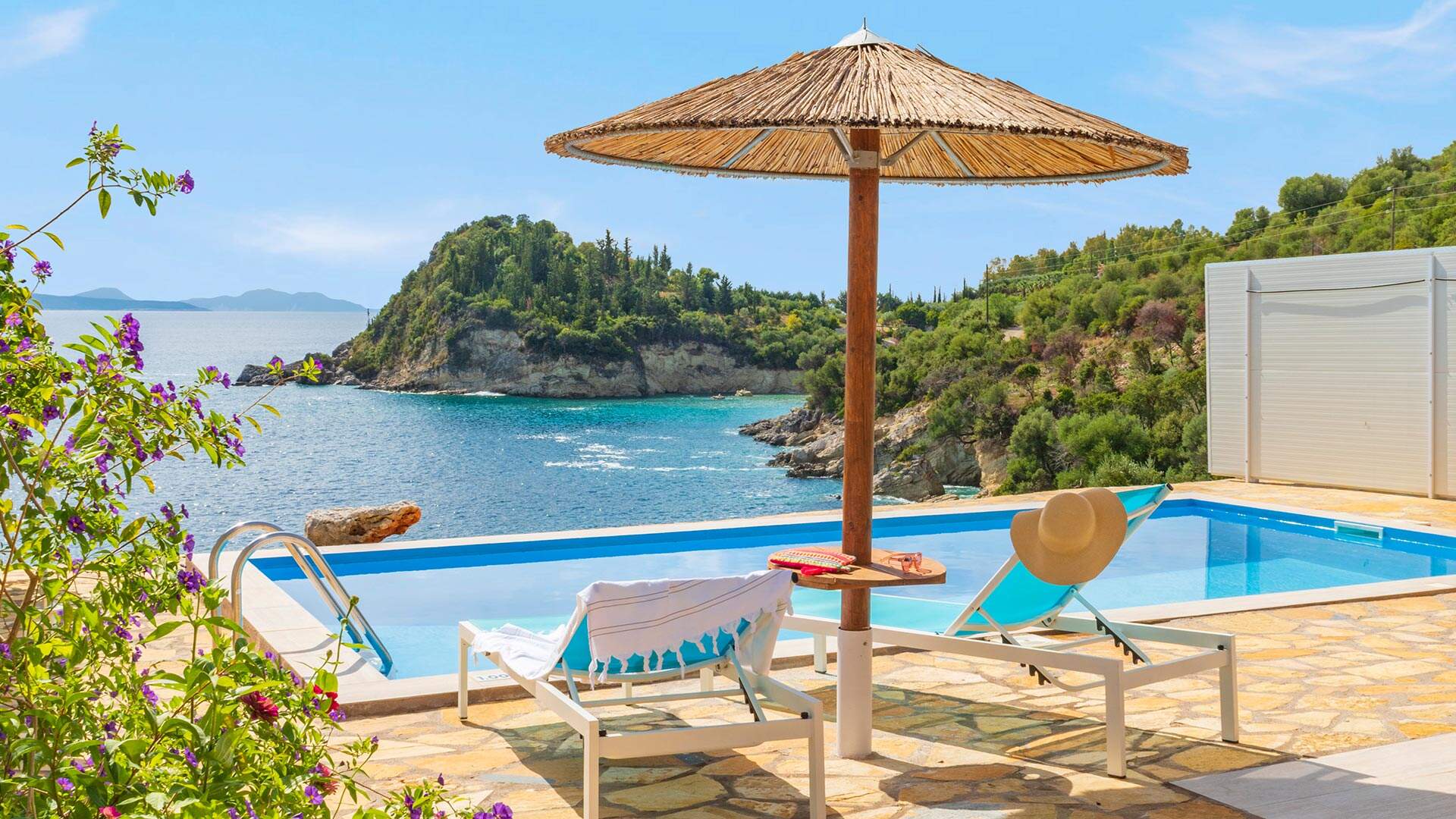 Terras met zwembad, ligstoelen en parasol met uitzicht op zee en bergen met bomen