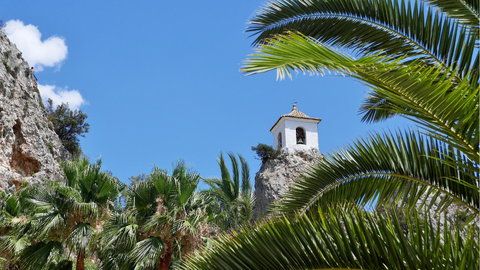 Strakblauwe lucht met rosten en palmbomen en uitzicht op een kerktorentje