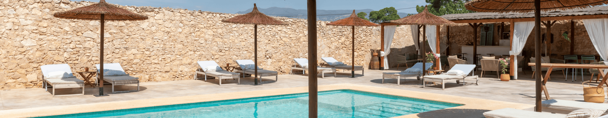 Stenen muur met ligbedden en rieten parasols bij een zwembad