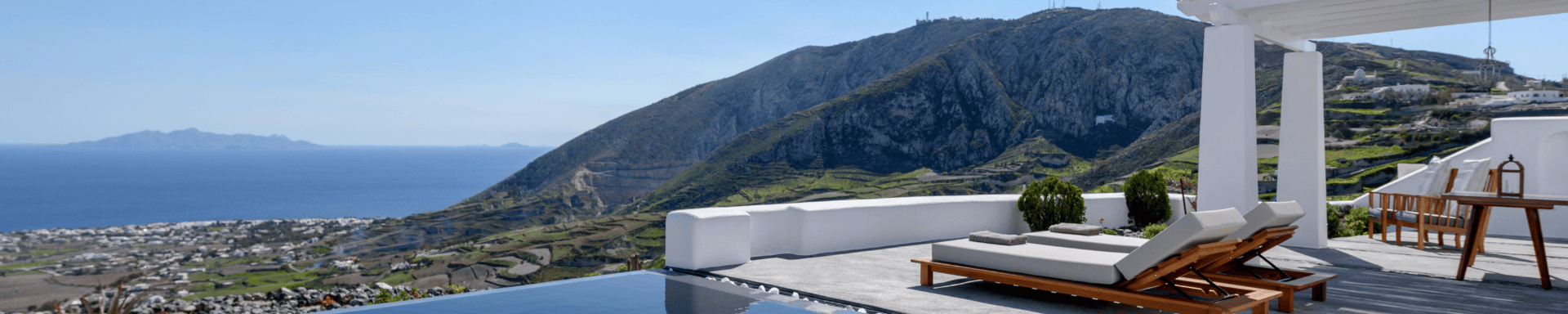 Luxe terras met ligstoelen, een infinity pool en panoramisch uitzicht op zee en bergen op Santorini.